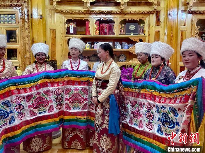 圖為女性展示村民自發(fā)繡制的“百米五彩哈達(dá)”?！±钣穹?攝